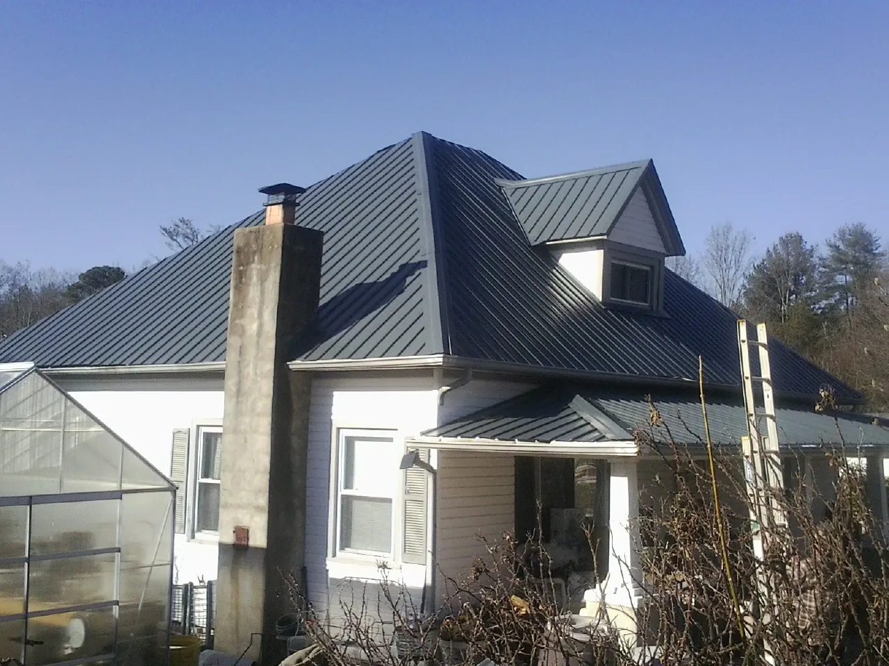 Dark blue standing seam metal roof on a white farmhouse with dormer — Slate & Tile Roof Repair by Roofing Brothers in Rutherford