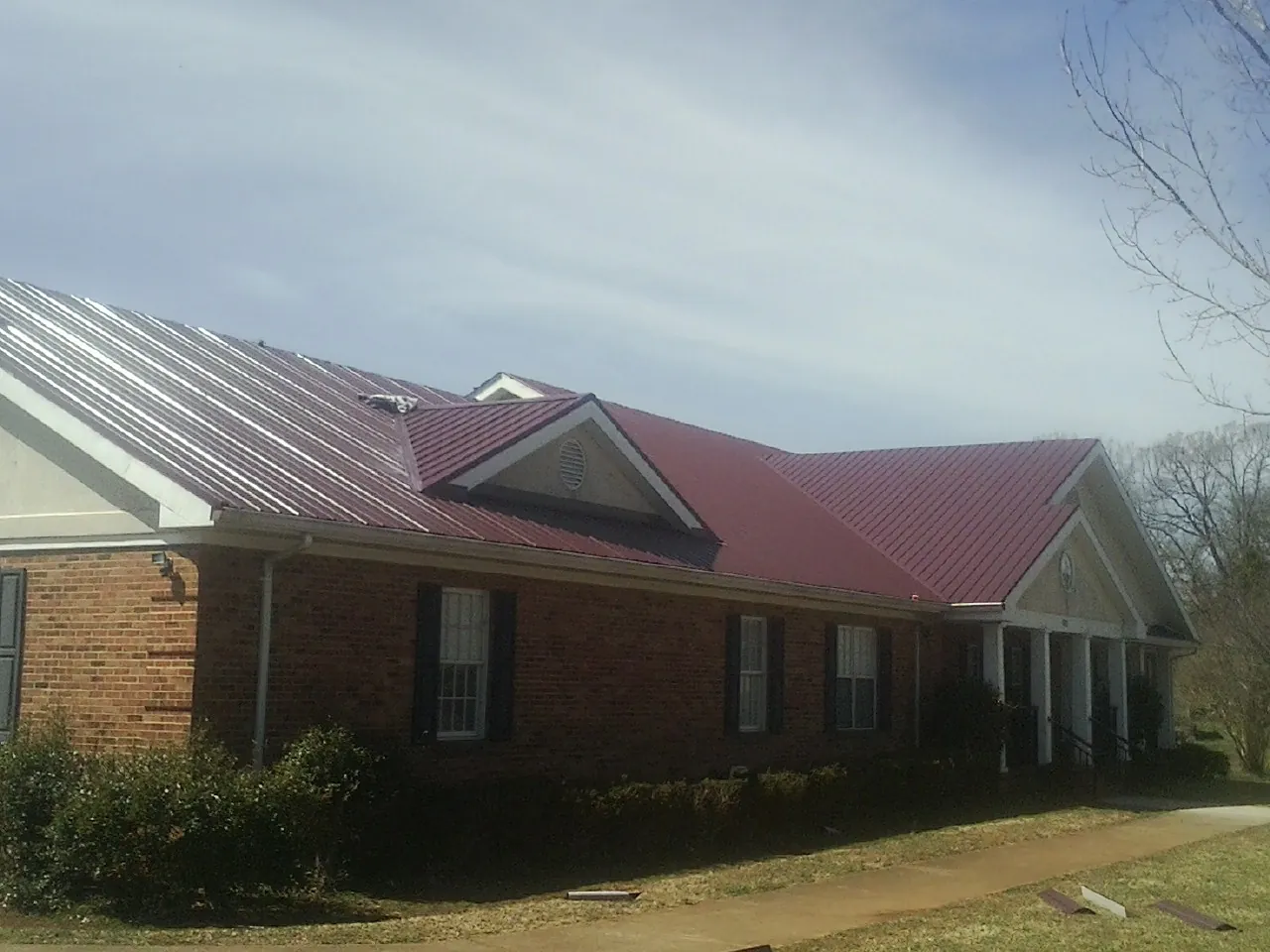 Red metal roof with gabled entries on a long brick building, from a Hail Damage Roof Repair job in Rutherford