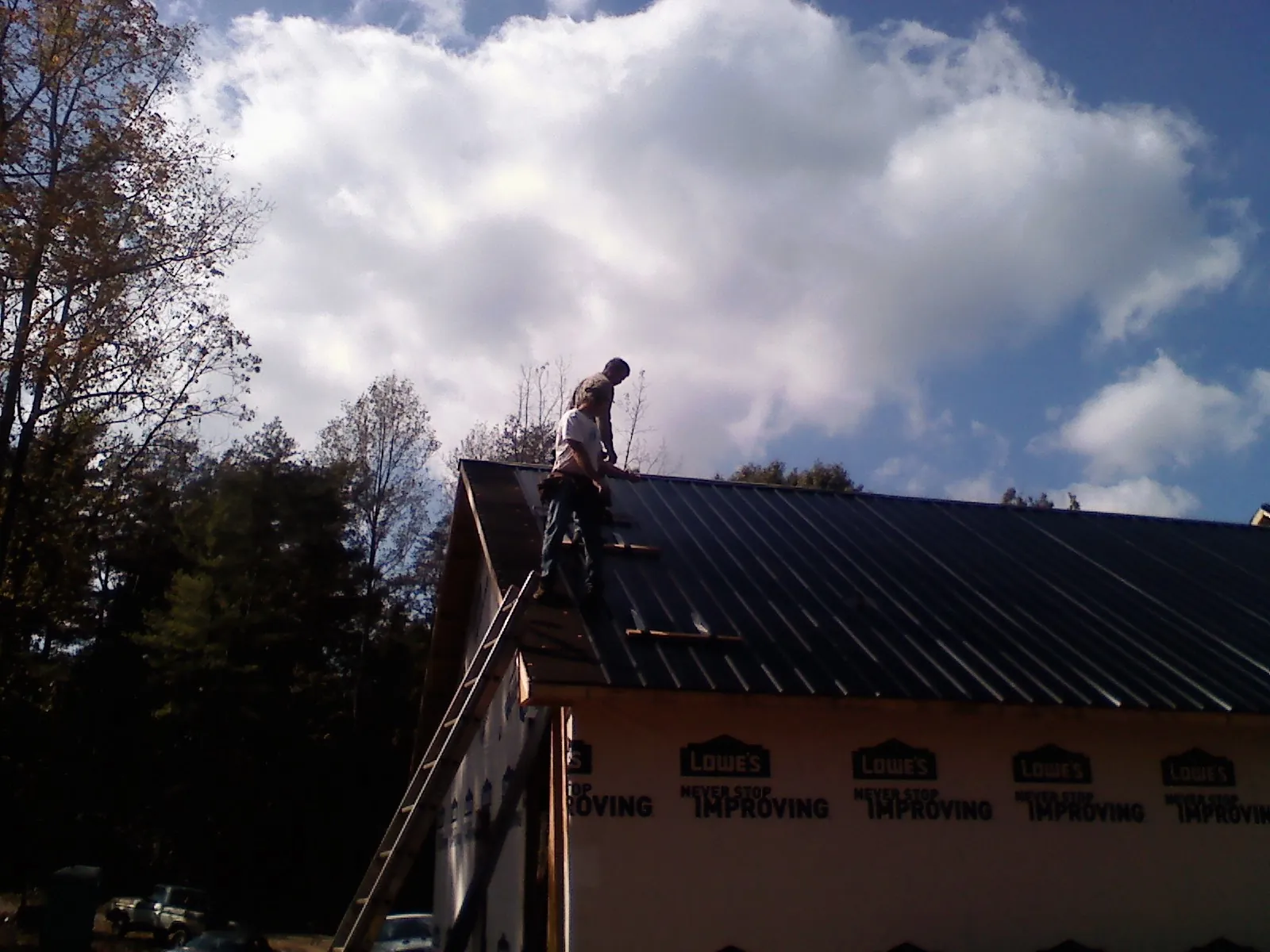 Roofer fastening dark metal panels high against a cloudy sky, from a Roof Inspection job in Rutherford